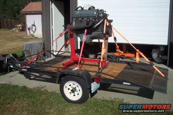 Engine on red stand secured with straps on a utility trailer with a license plate