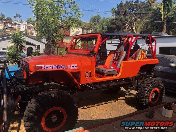 Orange Jeep Wrangler with "GENERAL LEE" and "01" graphics, roll cage, and racing seats