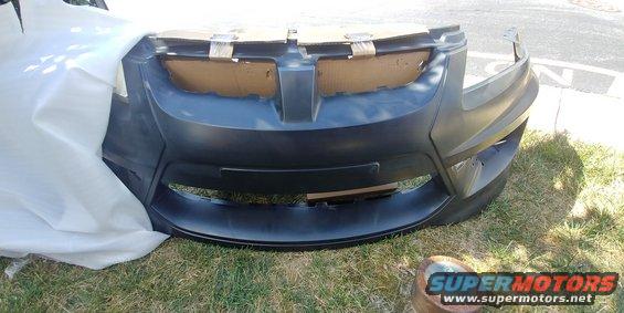 Unpainted front bumper cover with cardboard inserts in grille area