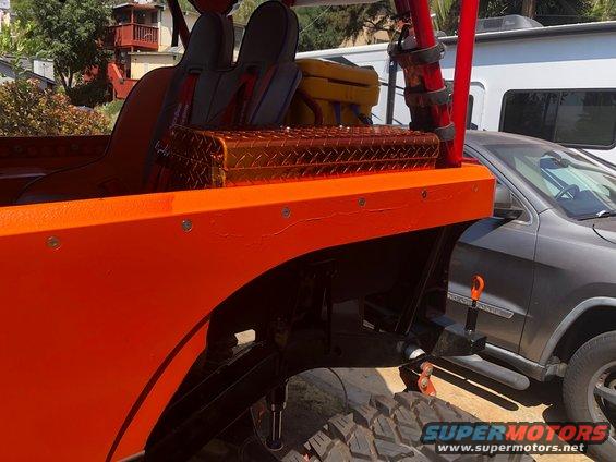 Orange off-road vehicle with racing seats and a toolbox in the bed, parked next to a gray SUV