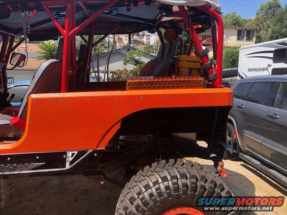 Orange off-road vehicle side view with large tires and roll cage