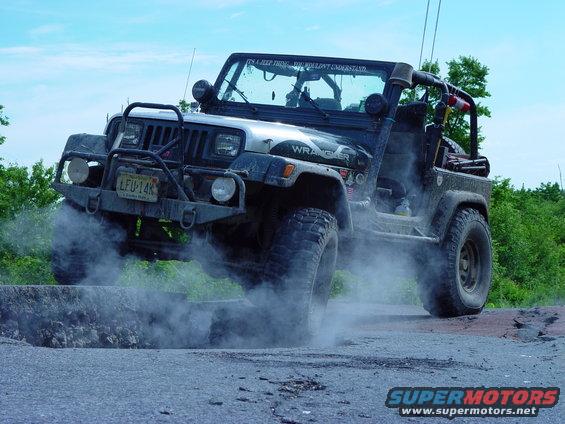 Jeep Wrangler driving over a rough patch of road, kicking up dust. License plate is LFU-14K