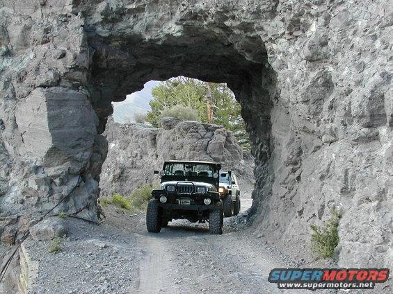 1992 Jeep Wrangler and another Jeep driving through a rock tunnel on a dirt road