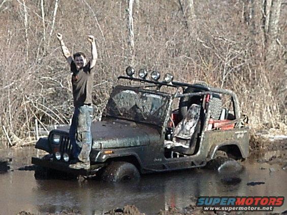 Man standing on a muddy 1992 Jeep Wrangler stuck in water with arms raised