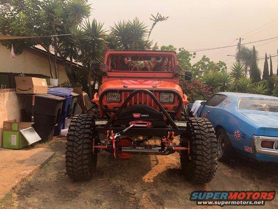 Orange Jeep Wrangler with winch and large off-road tires, parked next to a blue car