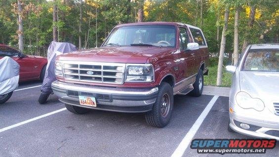 Maroon Ford Bronco parked in a lot next to a silver Mercedes and a covered red car