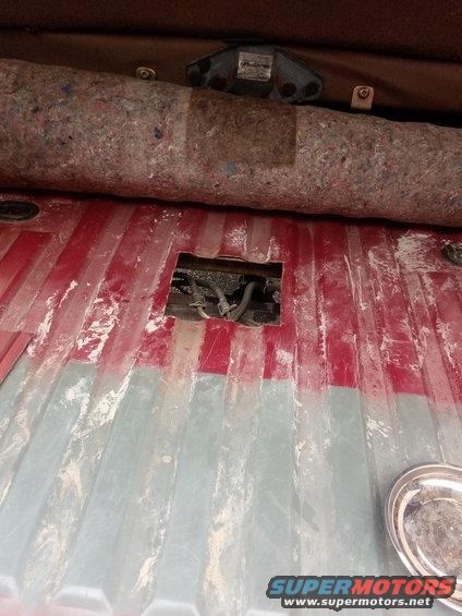 View of the cargo area floor with a cut-out revealing hoses and wiring