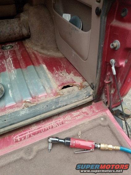 red vehicle interior showing rust hole in floor and an air ratchet on the tailgate