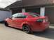 2009 Holden Commodore - Rear view of a red sedan with aftermarket wheels and tinted taillights parked outside a residential garage.