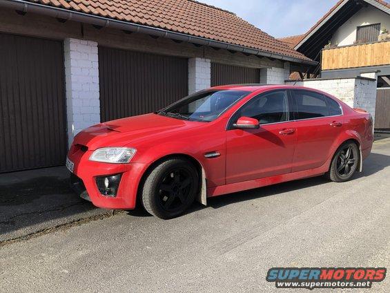 Red sedan with black wheels and a hood scoop, parked on a street