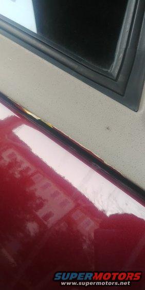 Red car door edge showing rust and a black rubber seal near a window