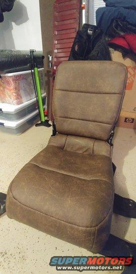 Brown car seat with horizontal stitching on backrest and seat cushion. Seat is in a garage with storage bins and a bike pump nearby