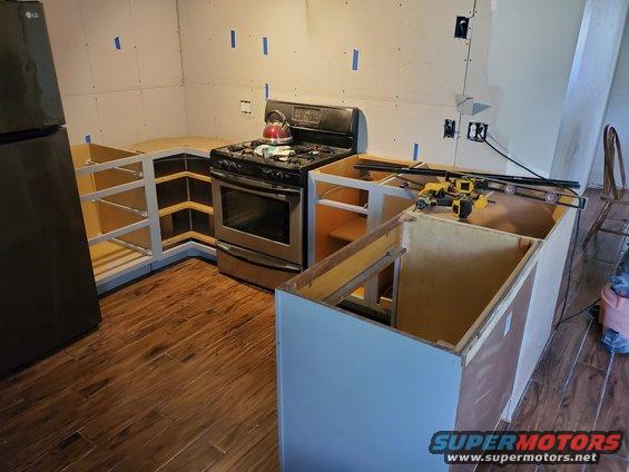 Kitchen under construction with cabinets, stove, refrigerator, and tools