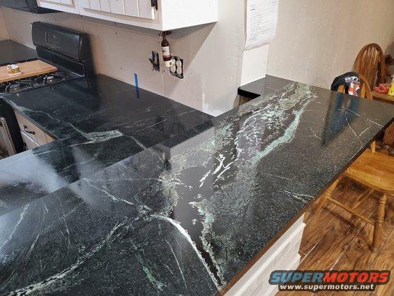 Kitchen countertop with dark green and white veining, visible stove and cabinets