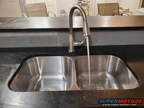 Double basin kitchen sink with a faucet running water into one side. Countertop is dark stone