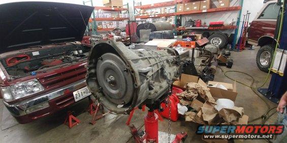 Transmission on stand next to red vehicle with hood open