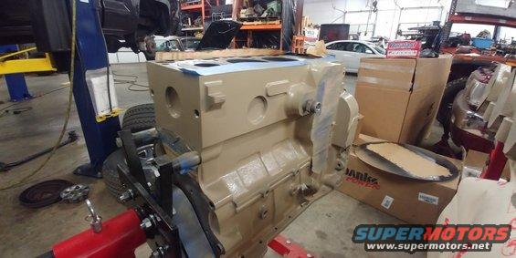 Engine block on red stand in garage, with boxes and car parts in background