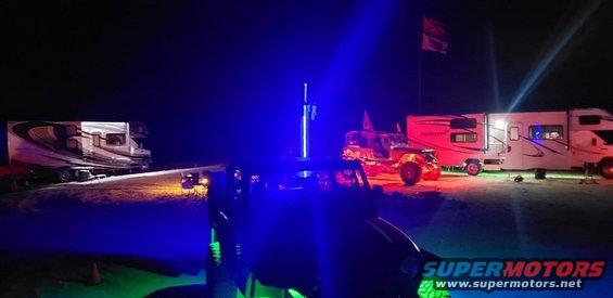 Off-road vehicle with blue and green lights at night, parked near RVs