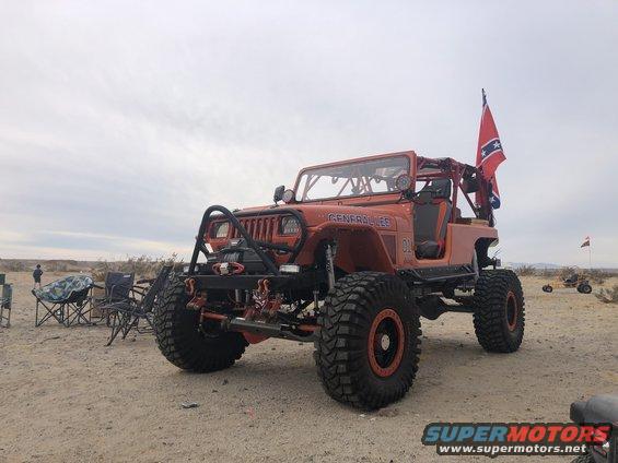 Orange Jeep Wrangler with "GENERAL LEE" text on the side, large off-road tires, and a roll cage. A Confederate flag is mounted on the back