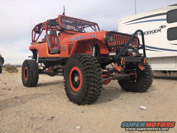 Orange Jeep Wrangler with "GENERAL LEE" text and "01" graphic, custom roll cage, large off-road tires, and winch