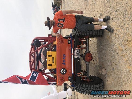 Man in orange shirt and hat leaning on a custom orange Jeep buggy with a Confederate flag. License plate reads 6JYF590