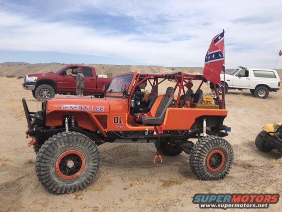 Orange Jeep CJ-7 with roll cage, large off-road tires, and "GENERAL LEE" text on the hood