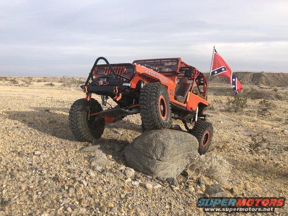 Orange off-road Jeep with roll cage and confederate flag on rock