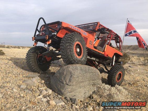 Orange Jeep Wrangler modified for off-roading, with "GENERAL LEE" text and "01" on the side, on a rock with a Confederate flag