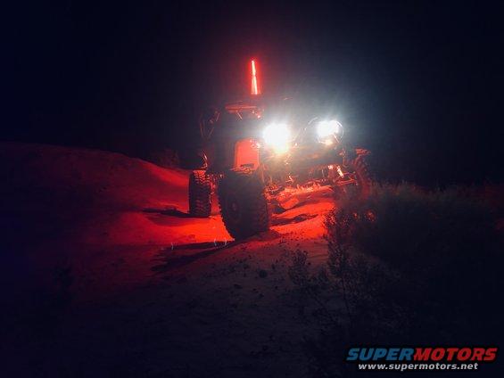 Off-road buggy with bright headlights and a red light bar, driving on a dirt hill at night