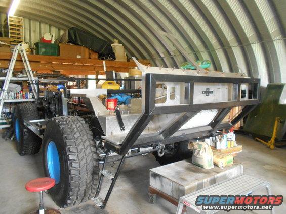Custom off-road vehicle chassis with large tires and blue rims, unfinished interior, in a workshop