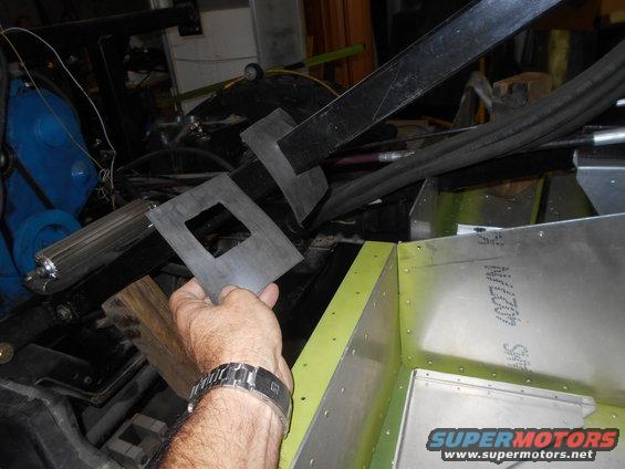 Hand holding a metal bracket with a square cutout over a partially assembled aluminum structure