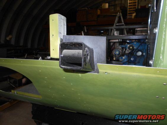 Close-up of a black tow hitch receiver mounted on a green vehicle body panel