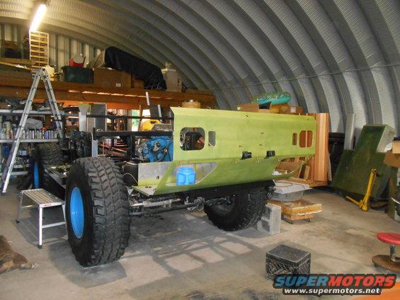 Off-road vehicle chassis with large tires and blue rims, partially assembled in a workshop