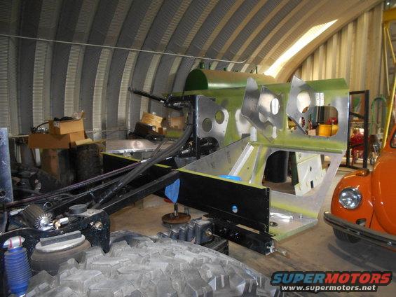 vehicle chassis being worked on in a garage, with an orange classic car visible on the right