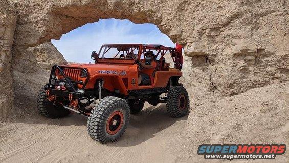 Orange Jeep Wrangler with 'General Lee' text on the side, driving through a rocky archway