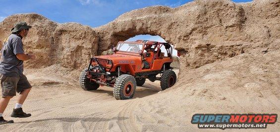 Orange 1992 Jeep Wrangler driving through a natural rock arch in a desert
