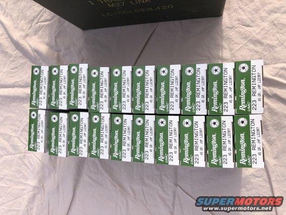 Rows of green Remington 223 ammunition boxes on a white cloth surface, with a dark green ammo can in the background