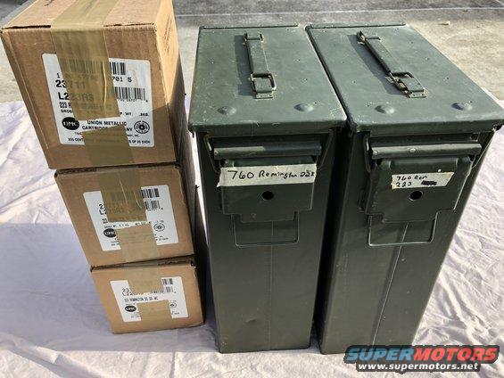 Two green metal ammo cans labeled '760 Remington .223' next to stacked cardboard boxes of ammunition