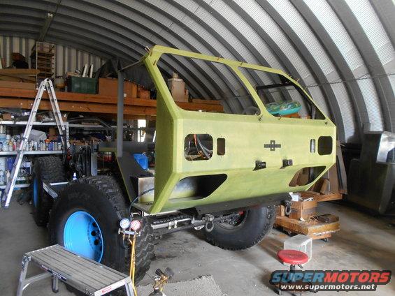 Custom off-road vehicle chassis with large tires and blue rims, undergoing construction