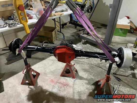 Rear axle assembly suspended by straps and resting on jack stands in a garage