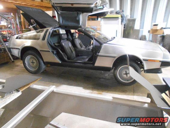 DeLorean DMC-12 with gullwing doors open, parked inside a garage