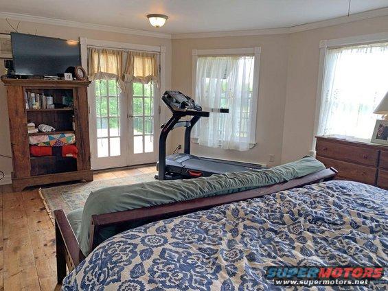 Bedroom with a treadmill, TV on a bookshelf, and double doors leading outside