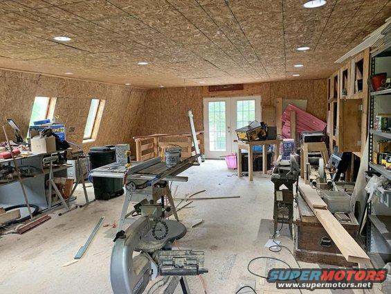 Workshop interior with table saw, miter saw, and other woodworking tools. Double doors lead outside