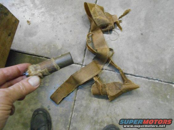 hand holding a metal part wrapped in fabric and twine, with a long strip of fabric on the ground