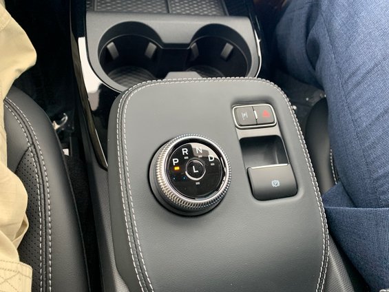 Car interior with a rotary gear selector showing 'P', 'R', 'N', 'D', 'L' and a black parking brake button