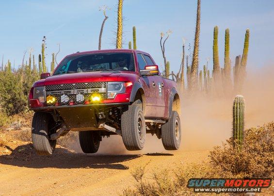 Red off-road truck mid-air jump on a dusty desert road with saguaro cacti