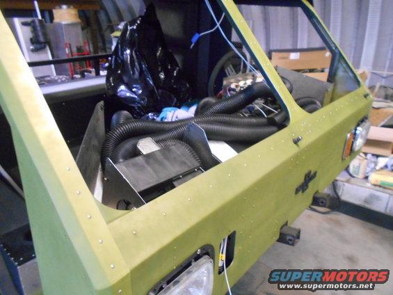 Interior view of a light green vehicle under construction, showing exposed engine components and black hoses