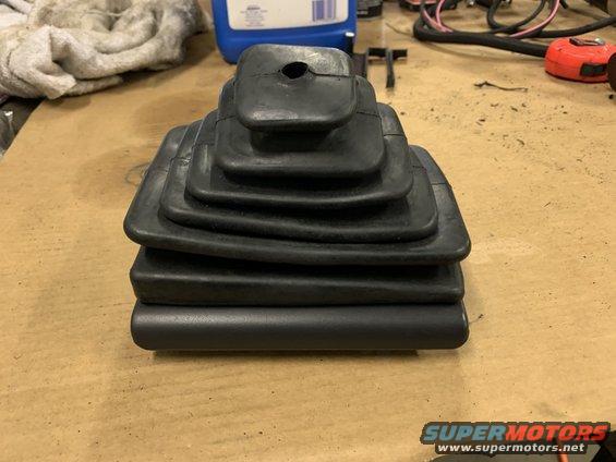 Black rubber shift boot with multiple accordion folds, resting on a wooden surface