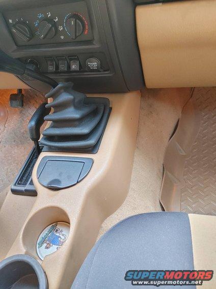 Jeep Cherokee interior showing center console with shifter, climate controls, and power outlet. There's a sticker in the cup holder