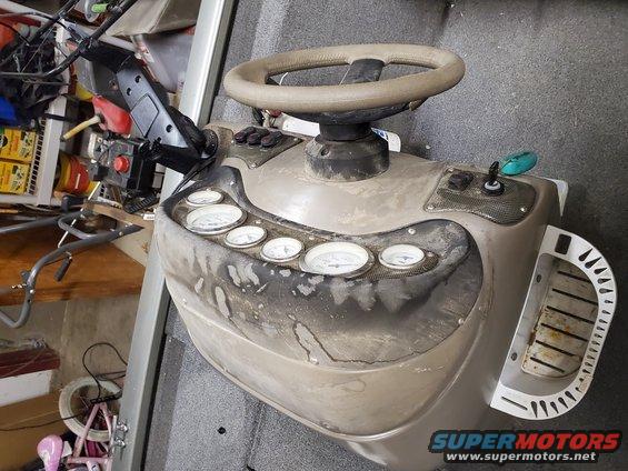 Boat console with beige steering wheel, multiple gauges, and black buttons. Some dirt and wear are visible